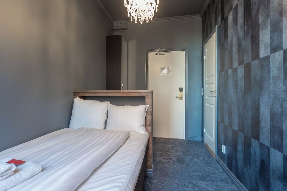 A hotel room with a bed, a chandelier, a door, and a wall with a checkered pattern.