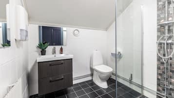 Un baño moderno con cabina de ducha de vidrio, inodoro blanco y tocador de madera oscura con espejo.