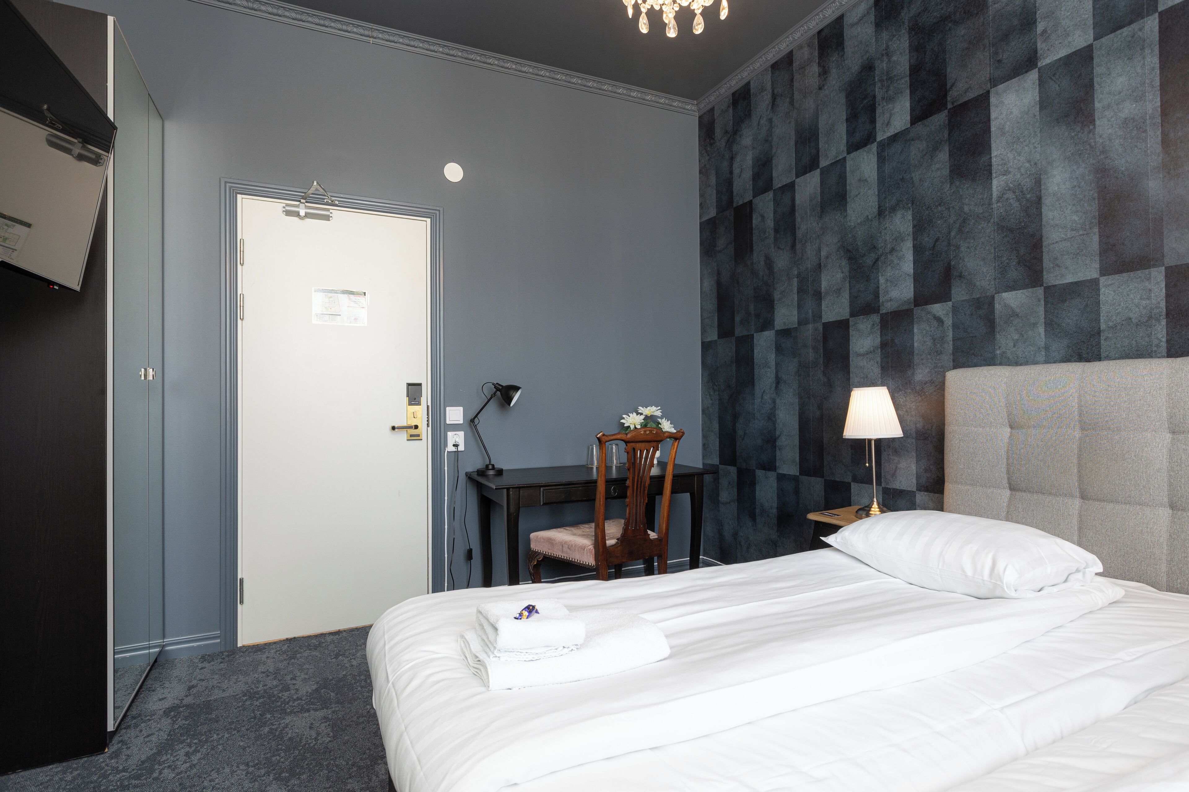 Una habitación de hotel con cama, escritorio, silla, lámpara y puerta.