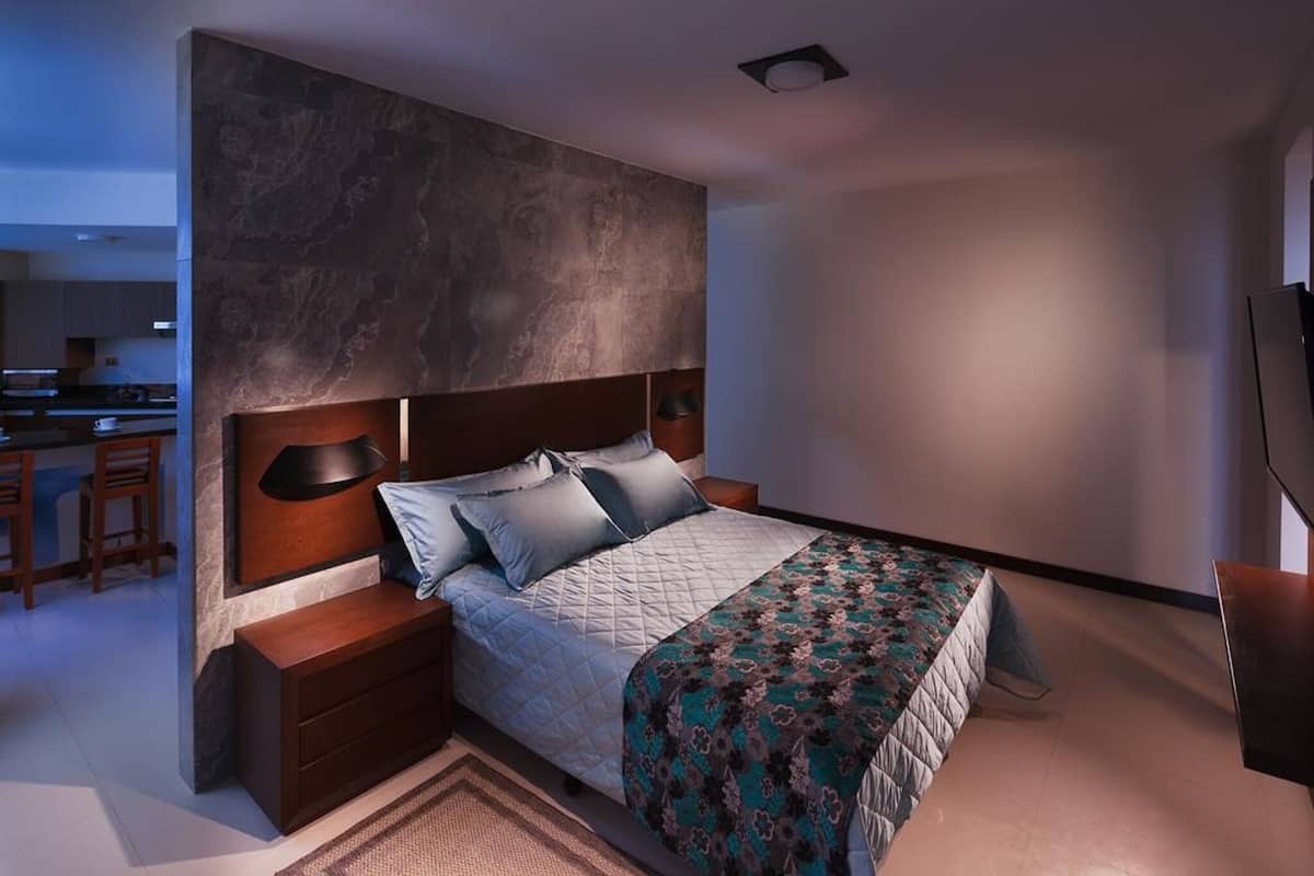 Un dormitorio moderno con una cama grande, cabecero de madera oscura, mesitas de noche y un banco empotrado.