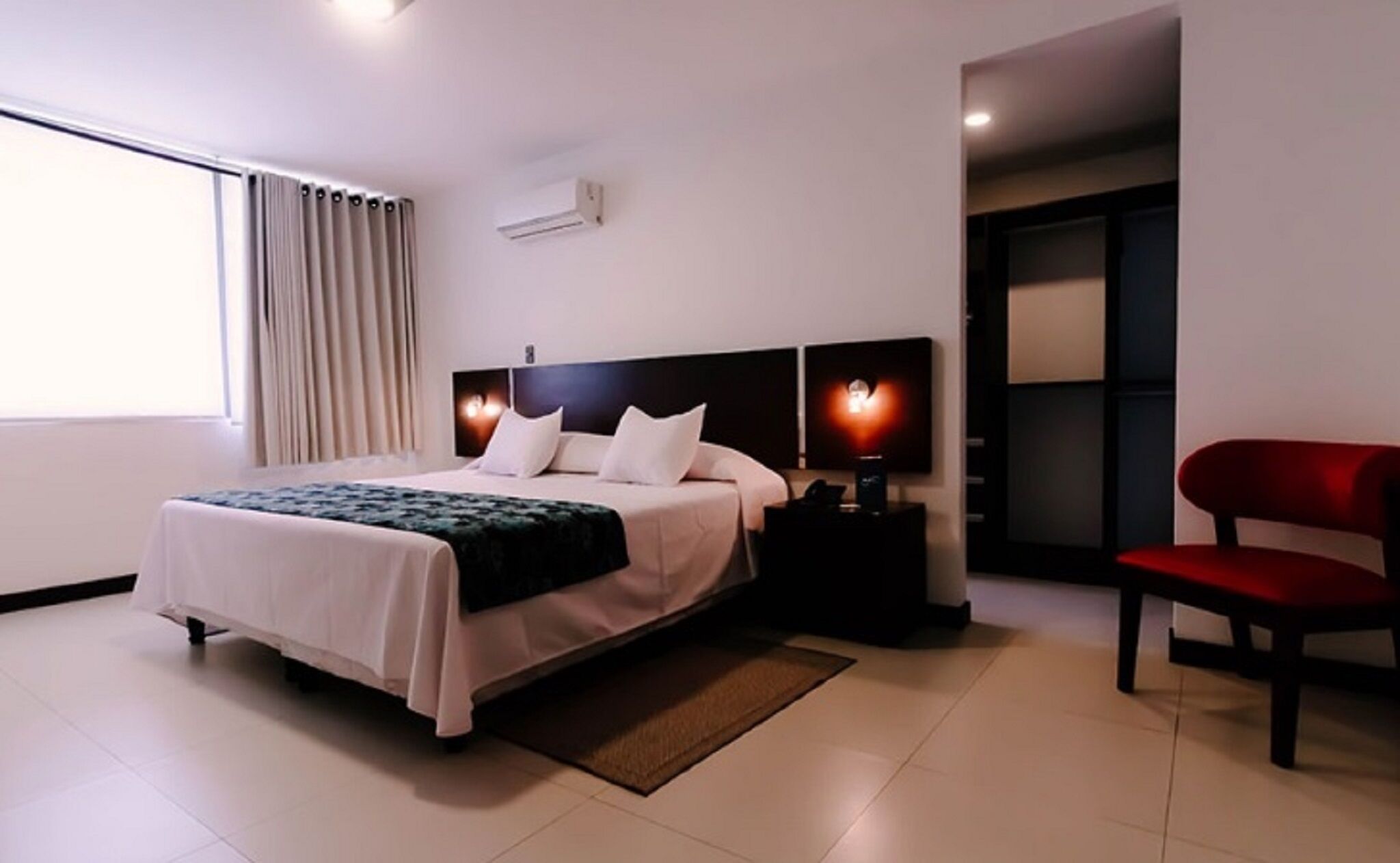A modern hotel room with a bed, bedside tables, a chair, and a view of the outside.