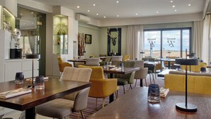 A modern dining area with multiple tables and chairs, a large window with a view, and a mounted deer head on the wall. - Hotel - Restaurant Crystal (Erstein)