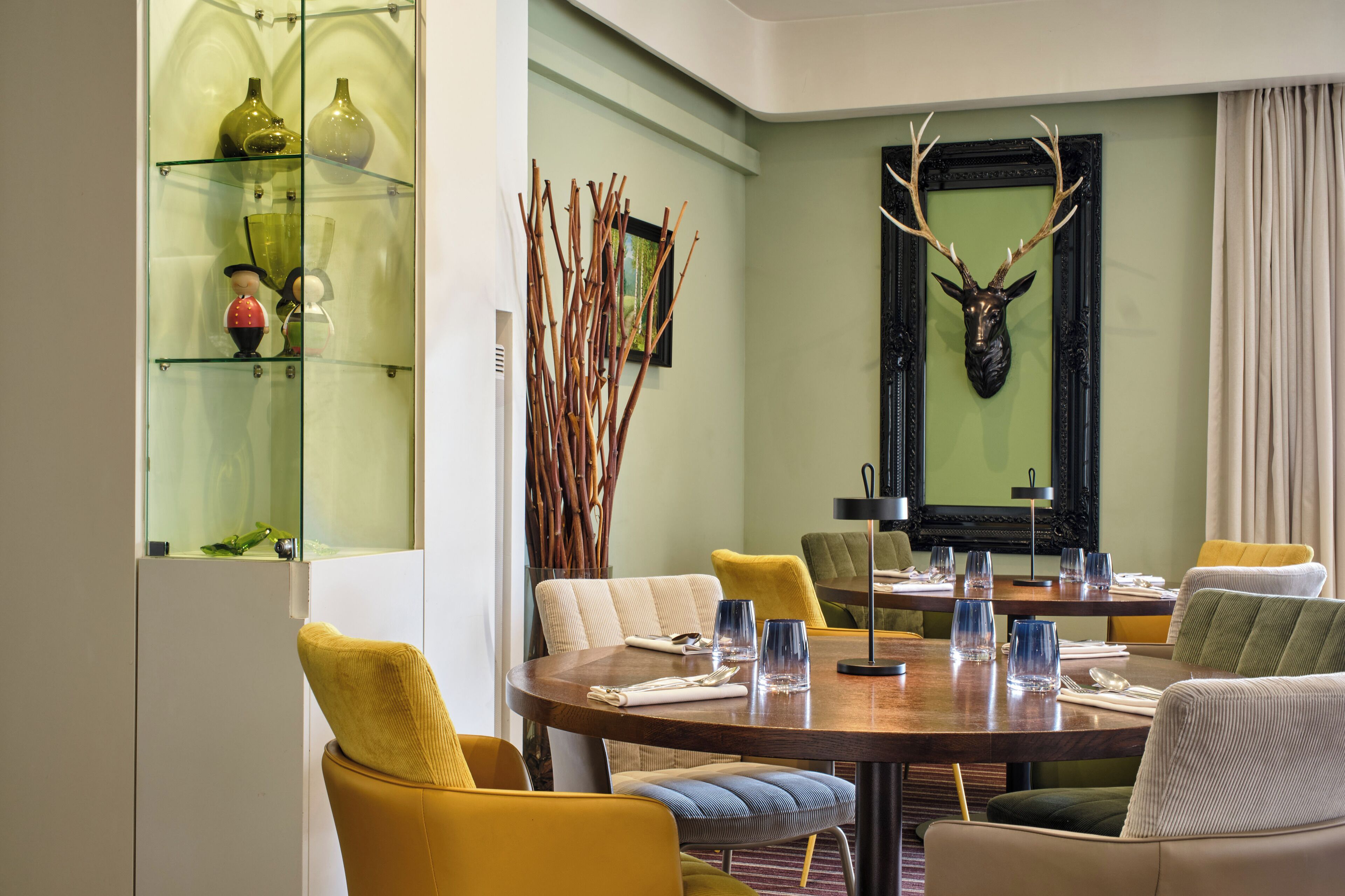 Un coin repas avec une table ronde, des chaises jaunes et une vitrine contenant des objets décoratifs.