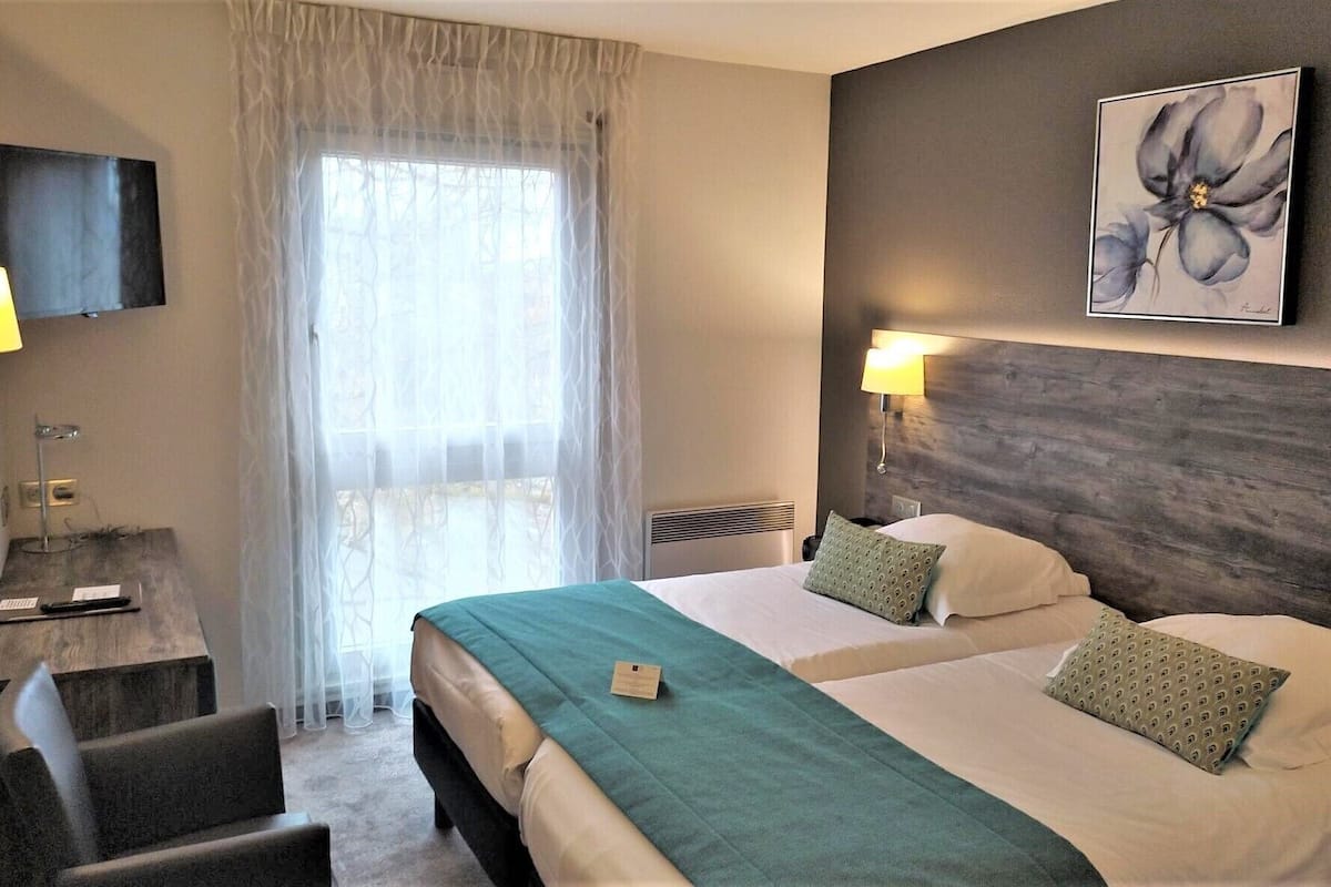 Habitación de hotel con dos camas, un escritorio, una silla, un televisor y una ventana con cortinas.