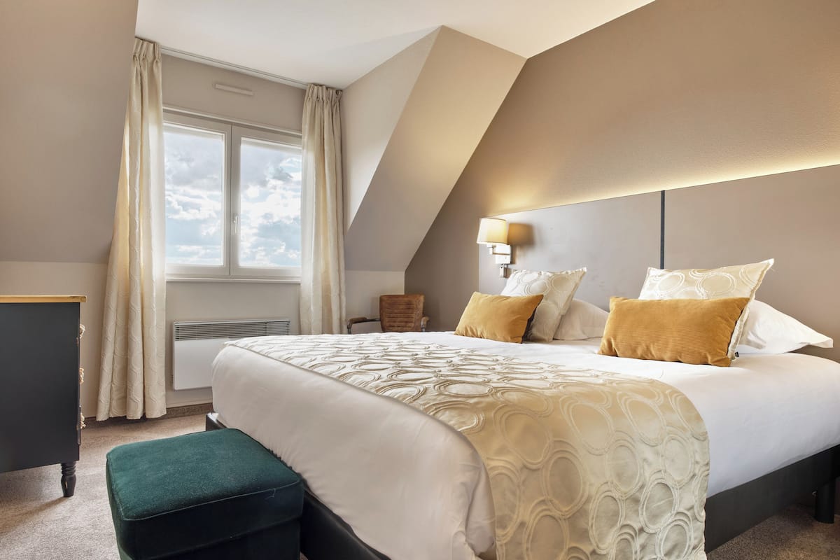Una habitación de hotel con una cama grande, un escritorio, una silla y una ventana con cortinas.