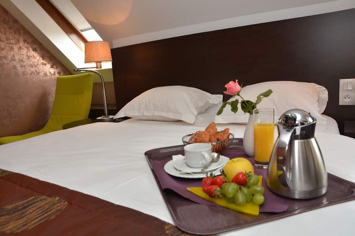 Una habitación de hotel con una cama, una bandeja de desayuno con frutas, una cafetera y una flor.