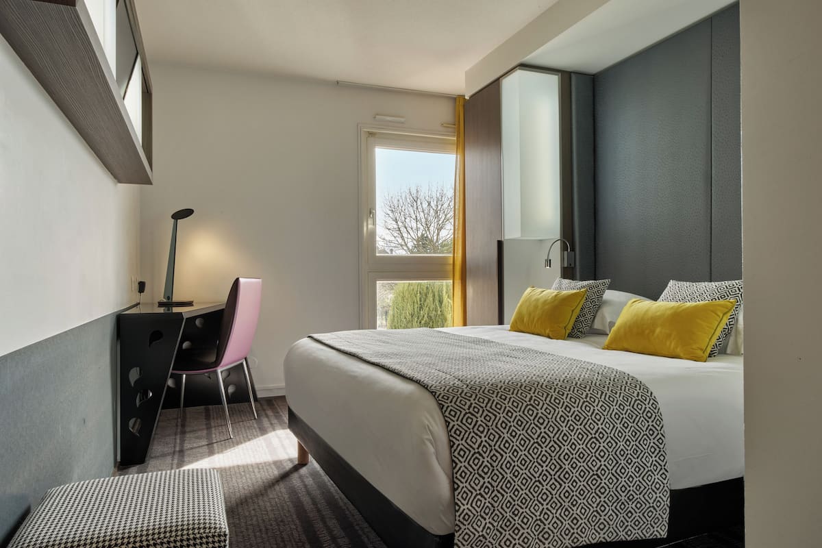 Una habitación de hotel moderna con cama, escritorio, silla y ventana.