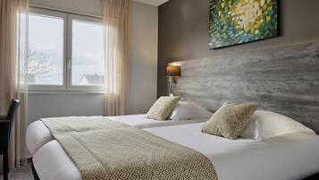 A hotel room with two beds, a large window with curtains, a wall-mounted lamp, and a piece of abstract art.