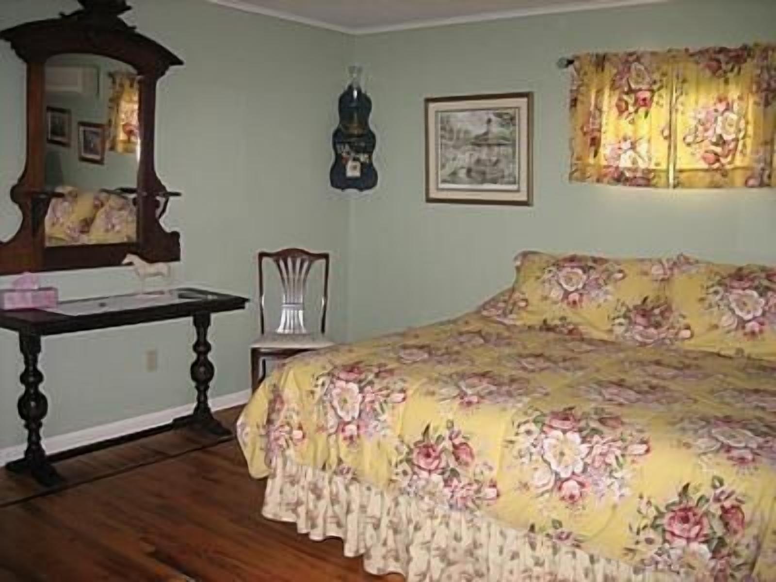 Un dormitorio con colcha estampada, cómoda de madera, espejo y un cuadro enmarcado en la pared.