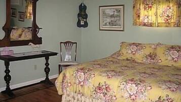 Un dormitorio con colcha estampada, cómoda de madera, espejo y un cuadro enmarcado en la pared.