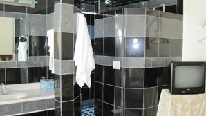 Um banheiro com paredes revestidas de azulejos pretos, uma toalha branca pendurada, uma pia e uma televisão sobre uma mesa.