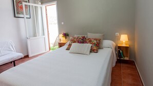 Quarto bem arrumado com uma cama, mesas de cabeceira, uma cadeira e uma porta que dá para uma área externa.