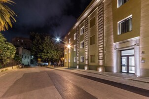 Vista nocturna de una calle con un edificio que destaca por su gran entrada y fachada iluminada.