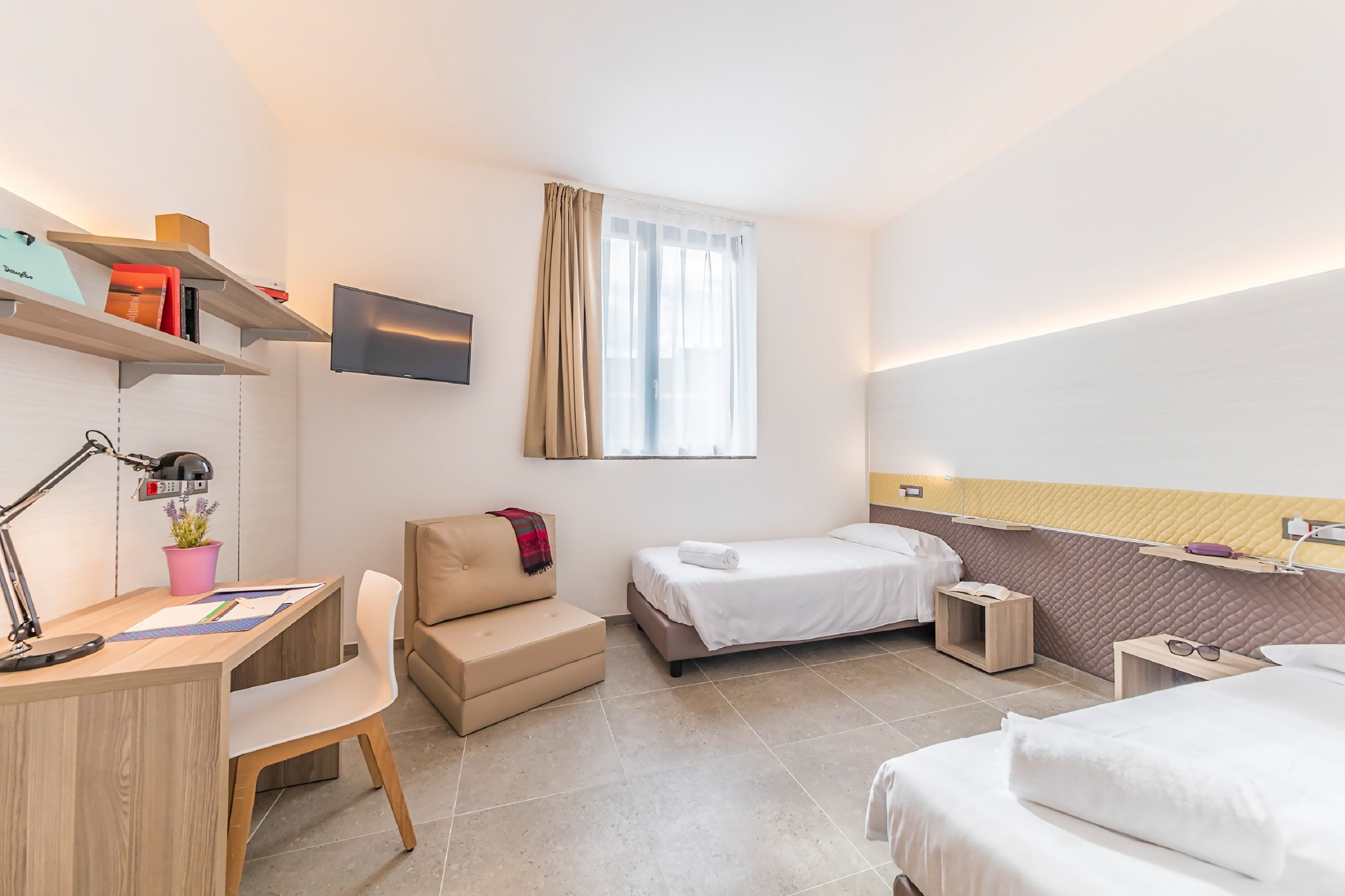 A modern hotel room with a desk, two beds, a TV, and a window with curtains.
