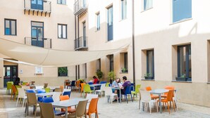 An outdoor café with tables and chairs, surrounded by a building with balconies and windows. - Camplus Palermo (Palermo)