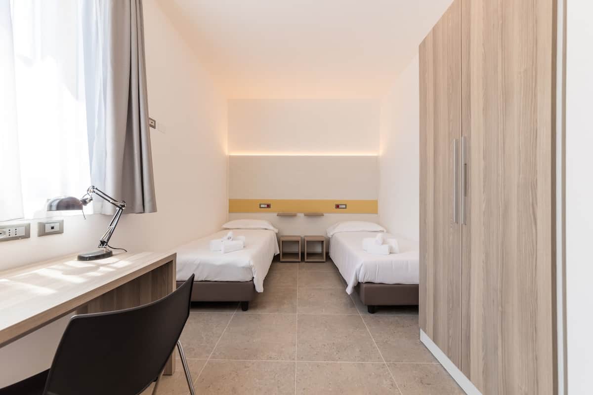 Une chambre d’hôtel avec deux lits, un bureau avec une chaise, une lampe et une armoire.