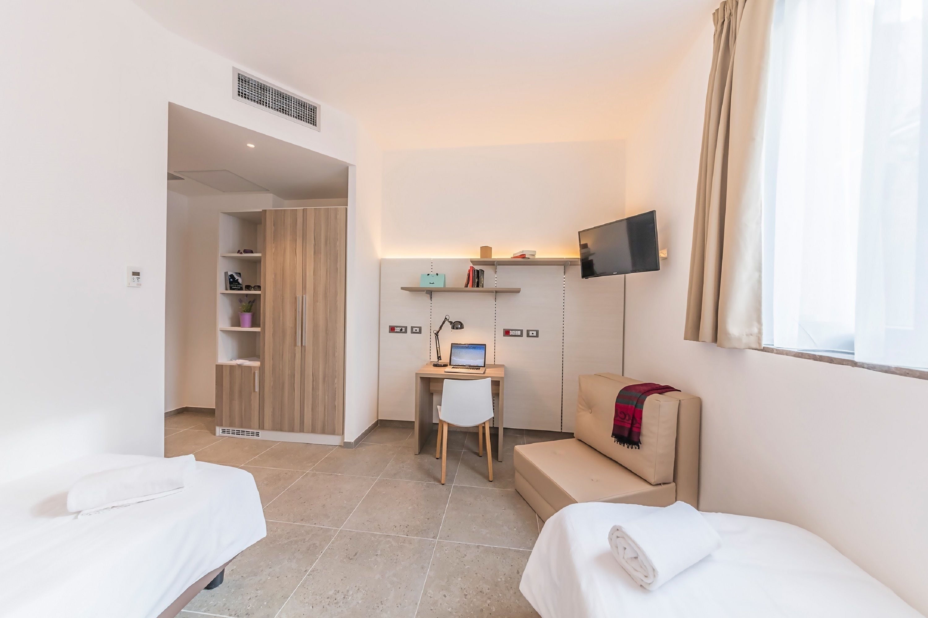 A hotel room with two beds, a desk with a computer, a TV, and a wardrobe.