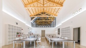 A spacious conference room with a high ceiling and exposed wooden beams, featuring a long table with chairs and a modern pendant light. - Camplus Palermo (Palermo)