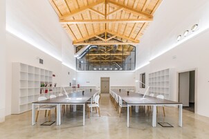 Una espaciosa sala de conferencias con techo alto y vigas de madera a la vista, que presenta una larga mesa con sillas y una moderna lámpara colgante.