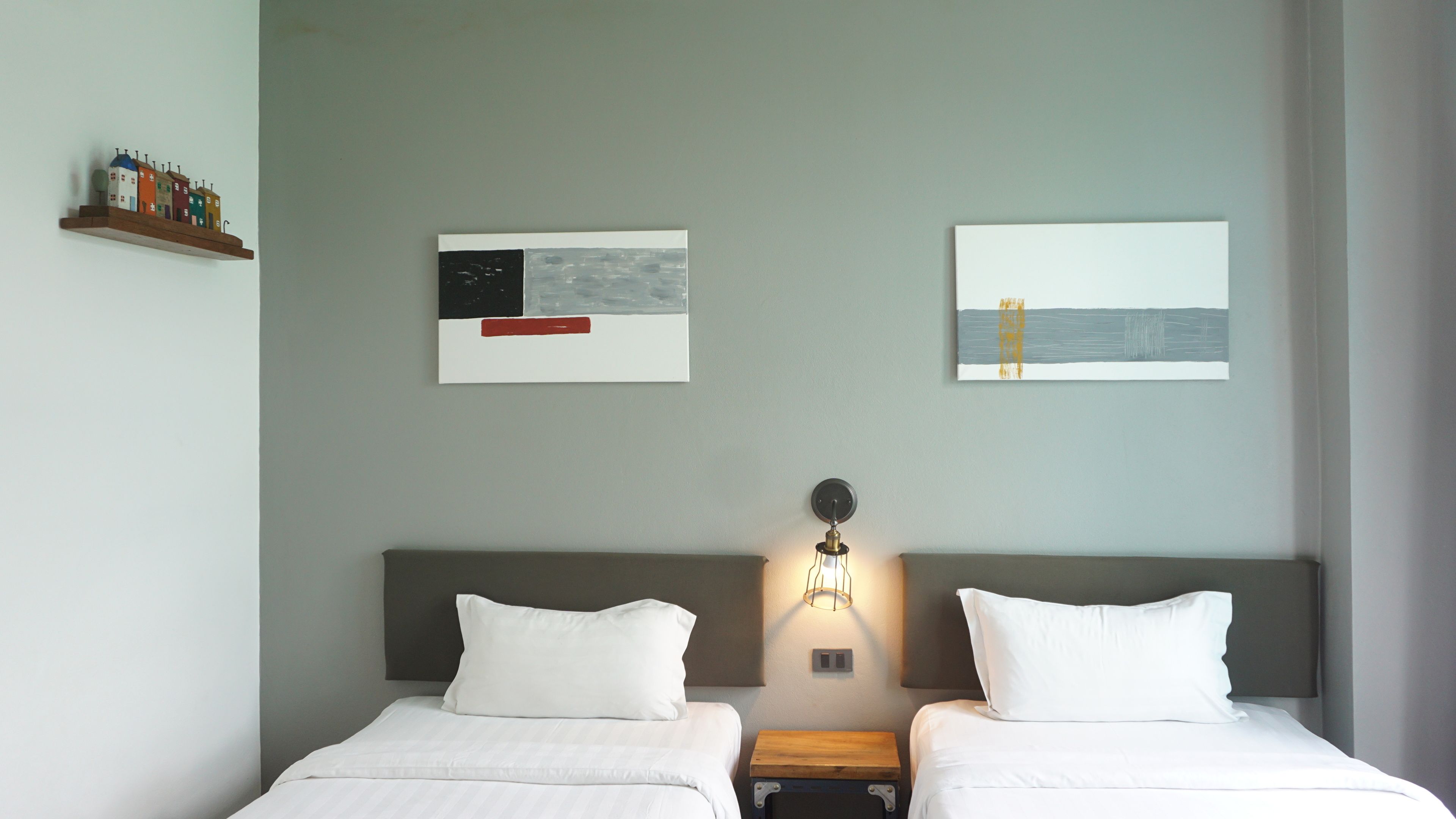Habitación de hotel con dos camas, una mesita de noche, una lámpara de pared y dos obras de arte.