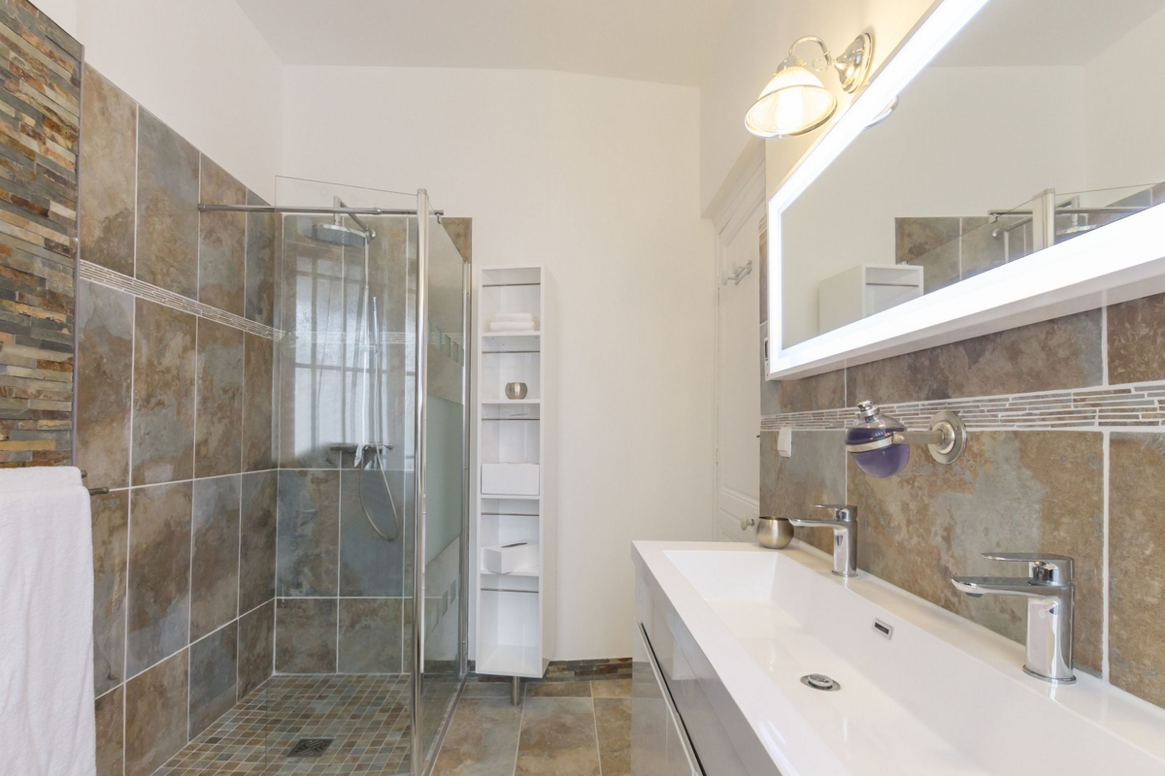 A modern bathroom with a glass shower enclosure, a large mirror, and a white vanity with two sinks.