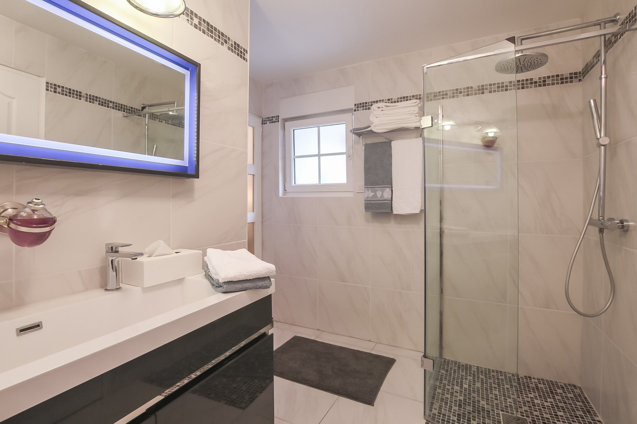 Une salle de bain moderne avec une douche à parois de verre, un grand miroir et un meuble-lavabo doté d’un porte-serviettes.