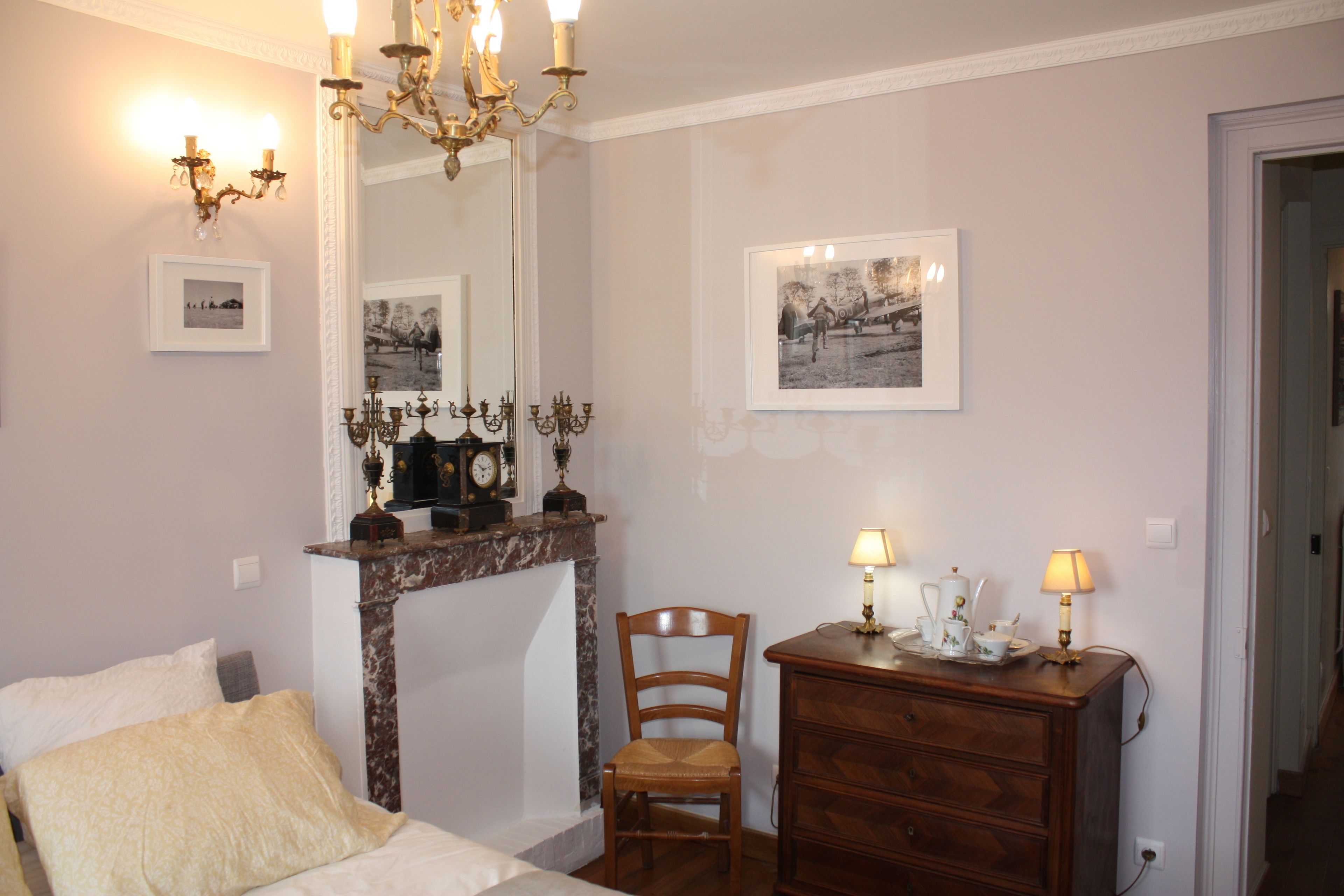 Un dormitorio con cama, cómoda de madera, silla, chimenea e iluminación en la pared.