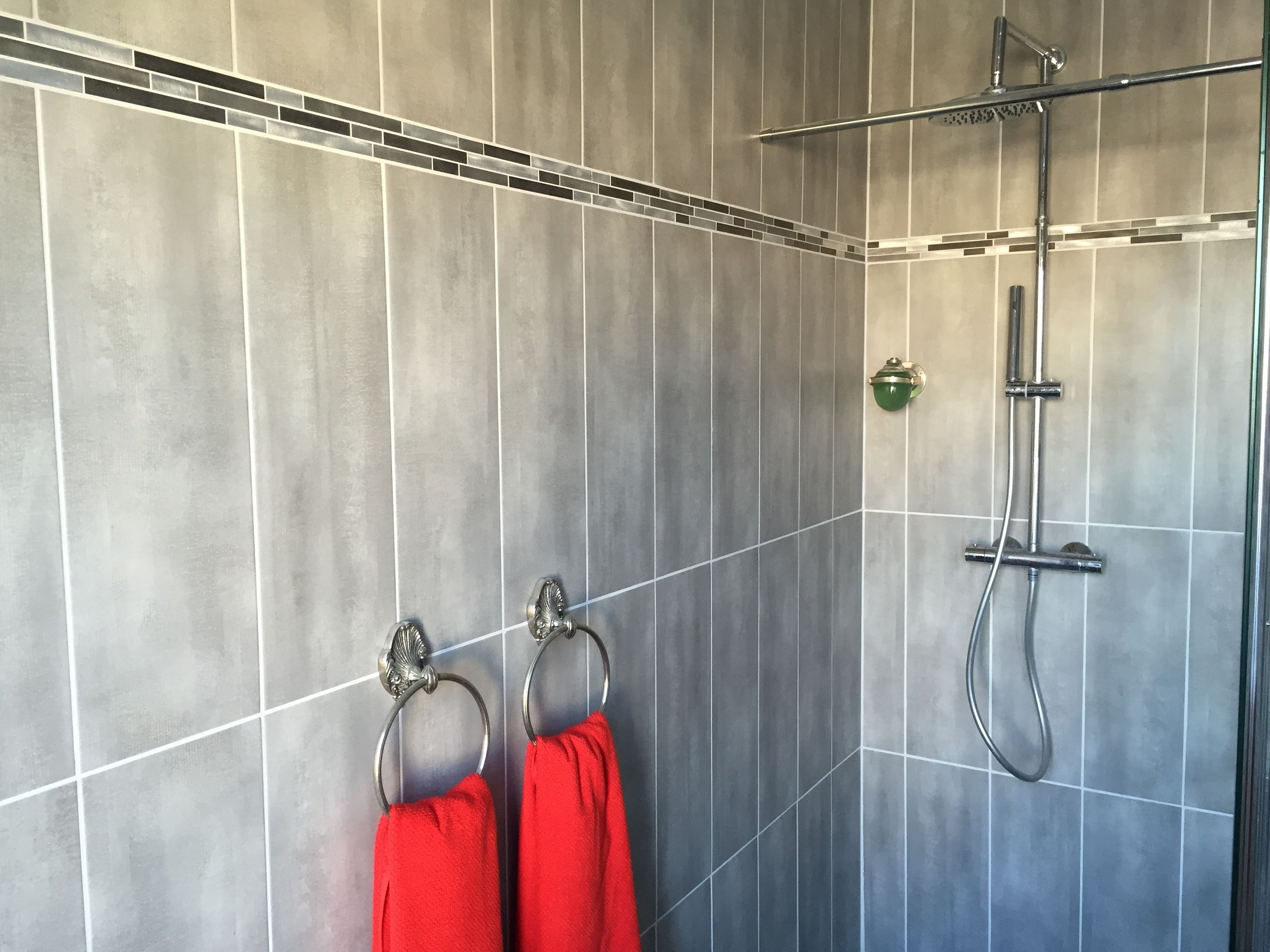 A modern bathroom with grey tiles, a glass shower enclosure, and two red towels hanging on metal rings.