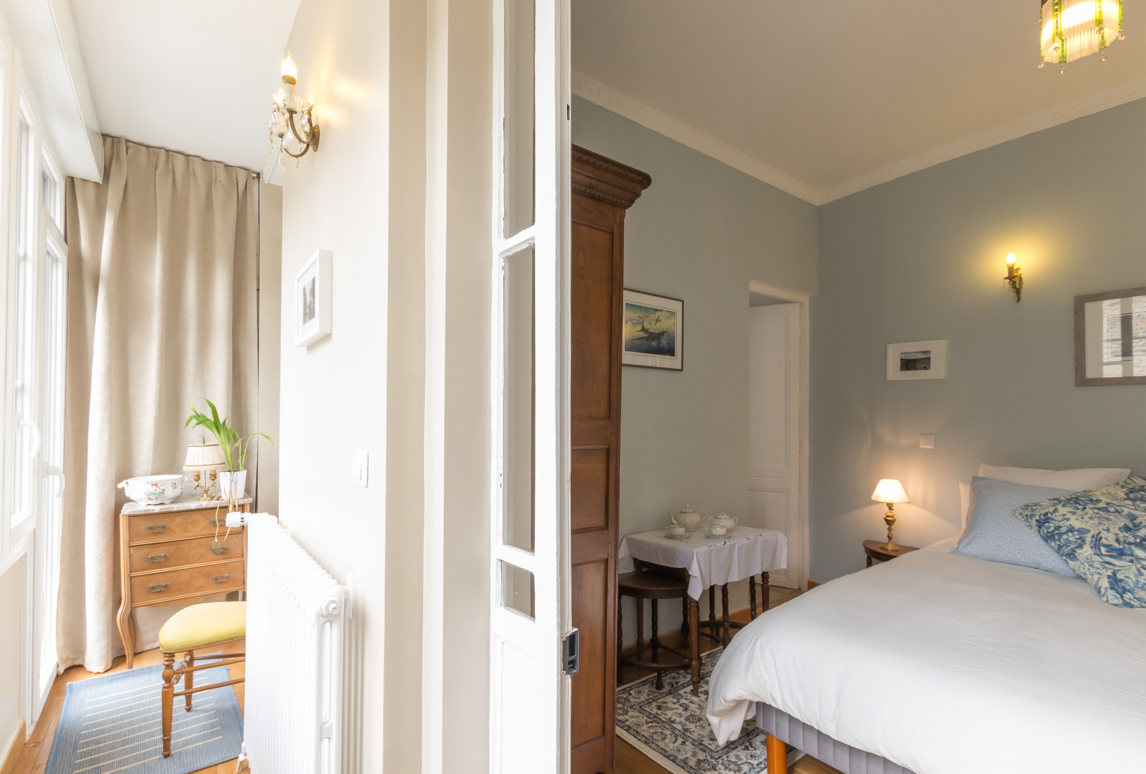 A bedroom with a bed, bedside table, lamp, and a view of a dining area with a table and chairs.