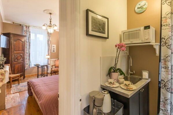 Une chambre d’hôtel comprenant un lit, un petit coin salon avec une chaise et une table, une kitchenette équipée d’un four à micro-ondes, d’une machine à café et d’un évier.