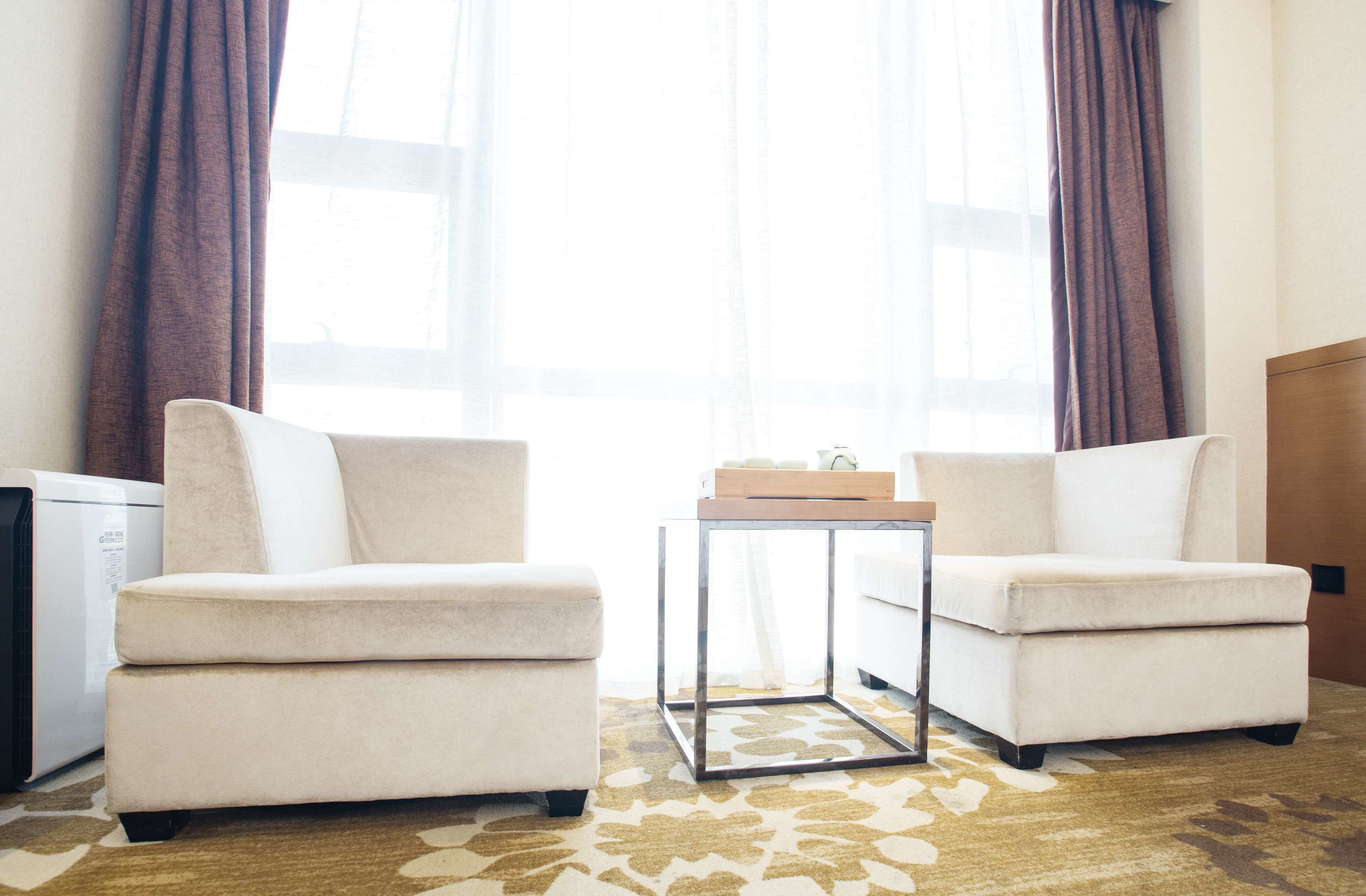 A hotel room with two white armchairs, a small table, and a large window with curtains.