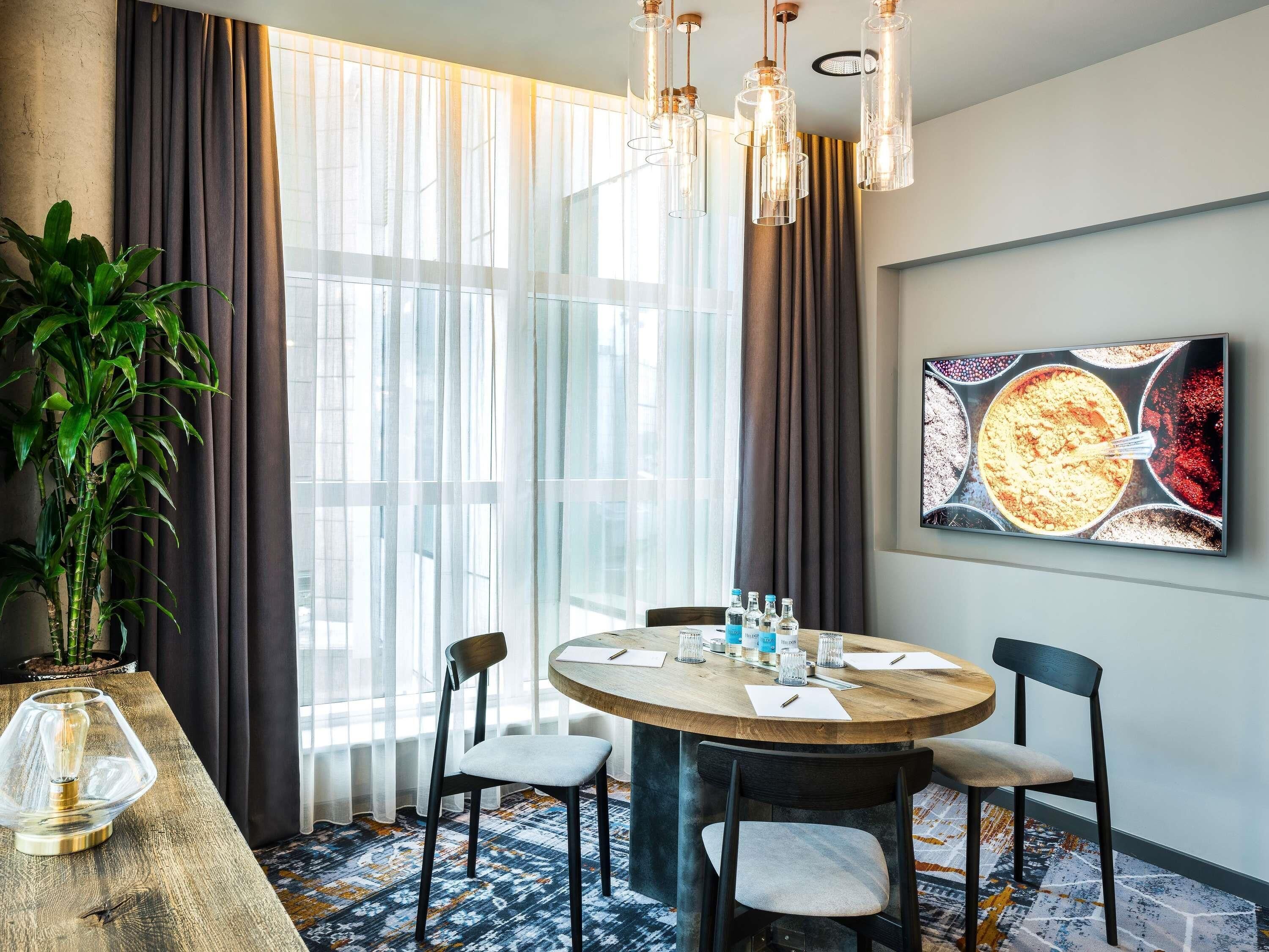 Un coin repas avec une table ronde, des chaises, une plante en pot et une grande fenêtre avec des rideaux.