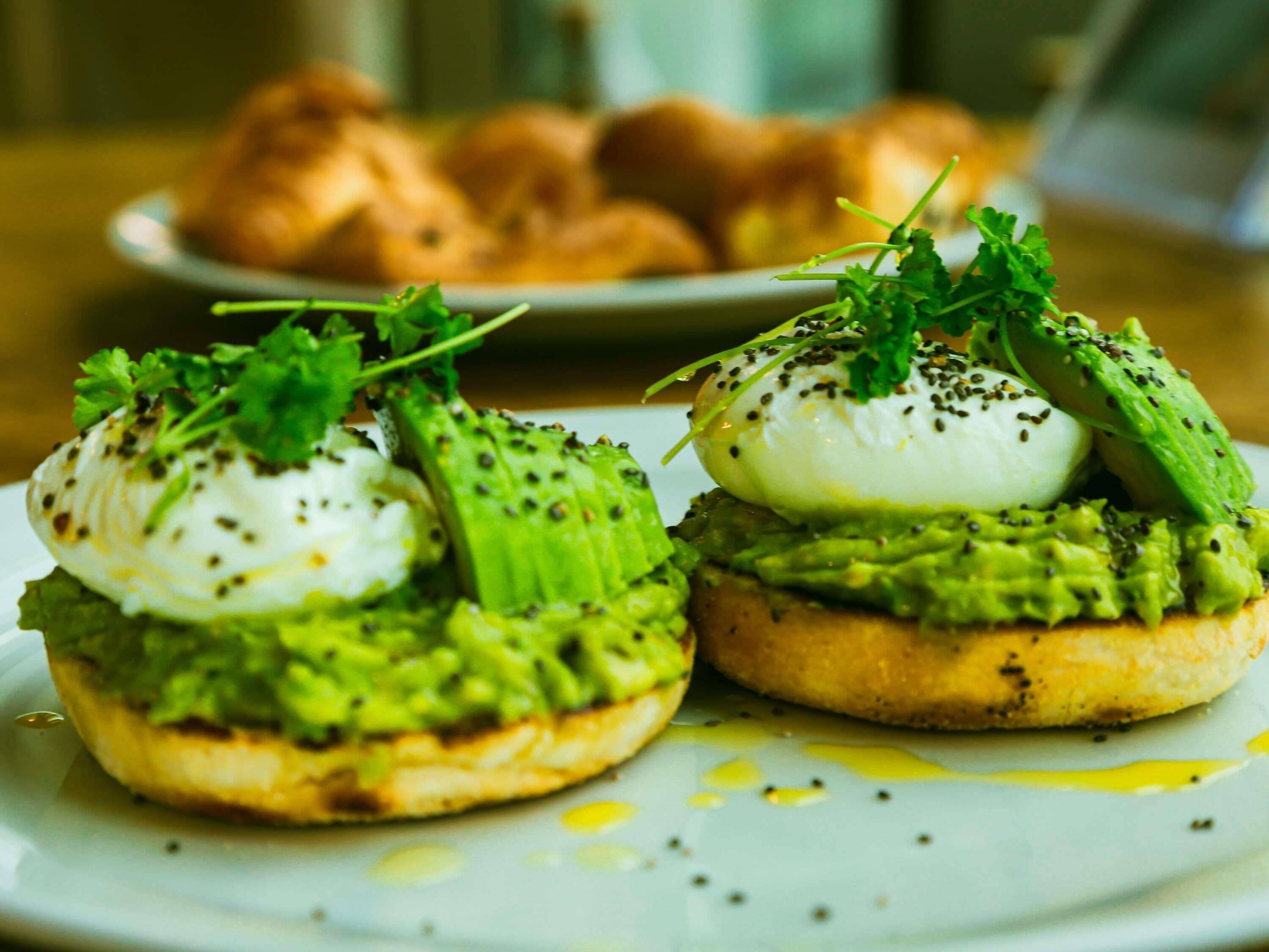 Two open-faced sandwiches with avocado and poached eggs on a plate.
