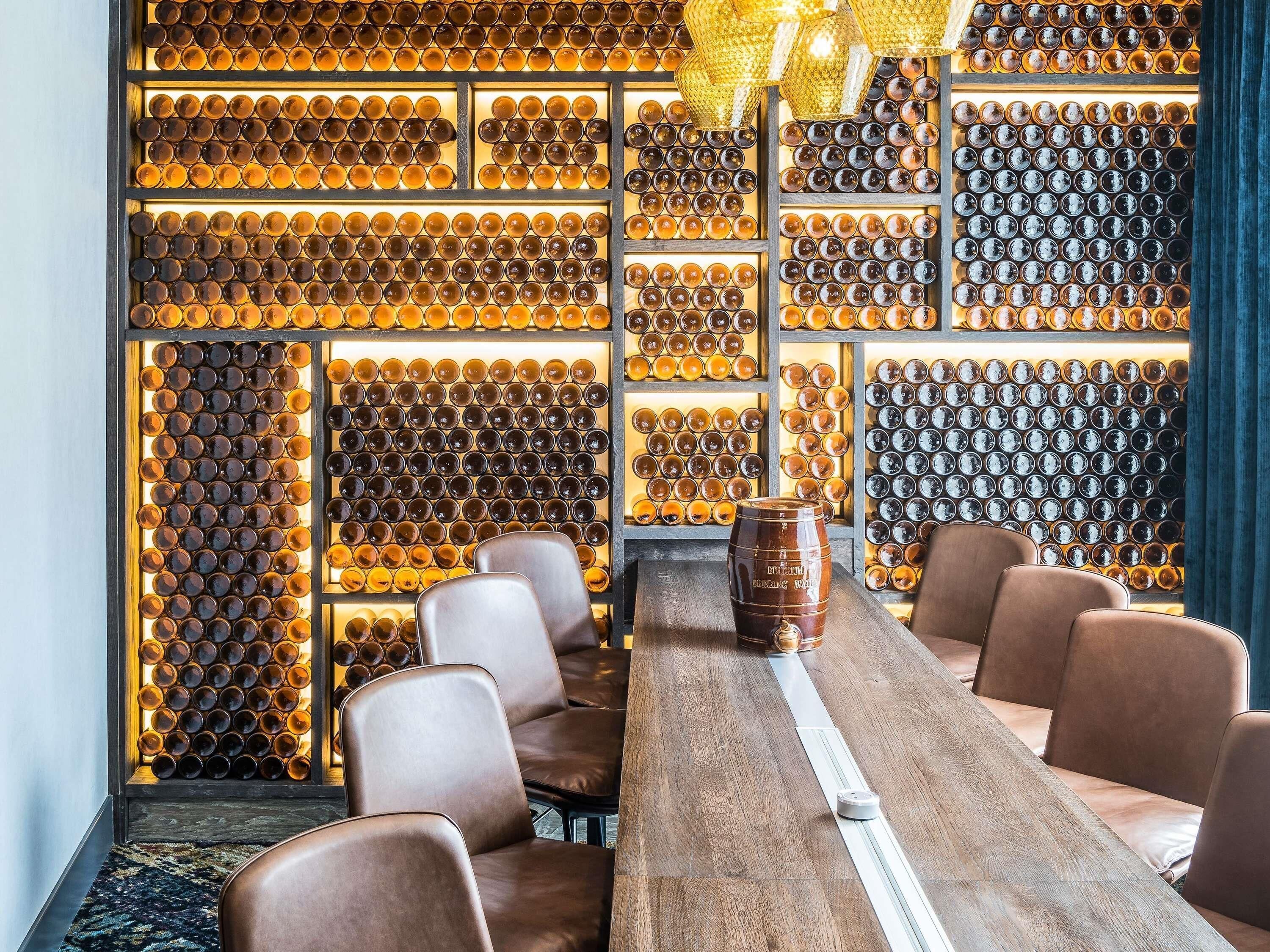 A bar area with a long wooden table, multiple chairs, and a wall of bottles.