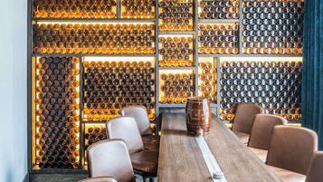 A bar area with a long wooden table, multiple chairs, and a wall of bottles.