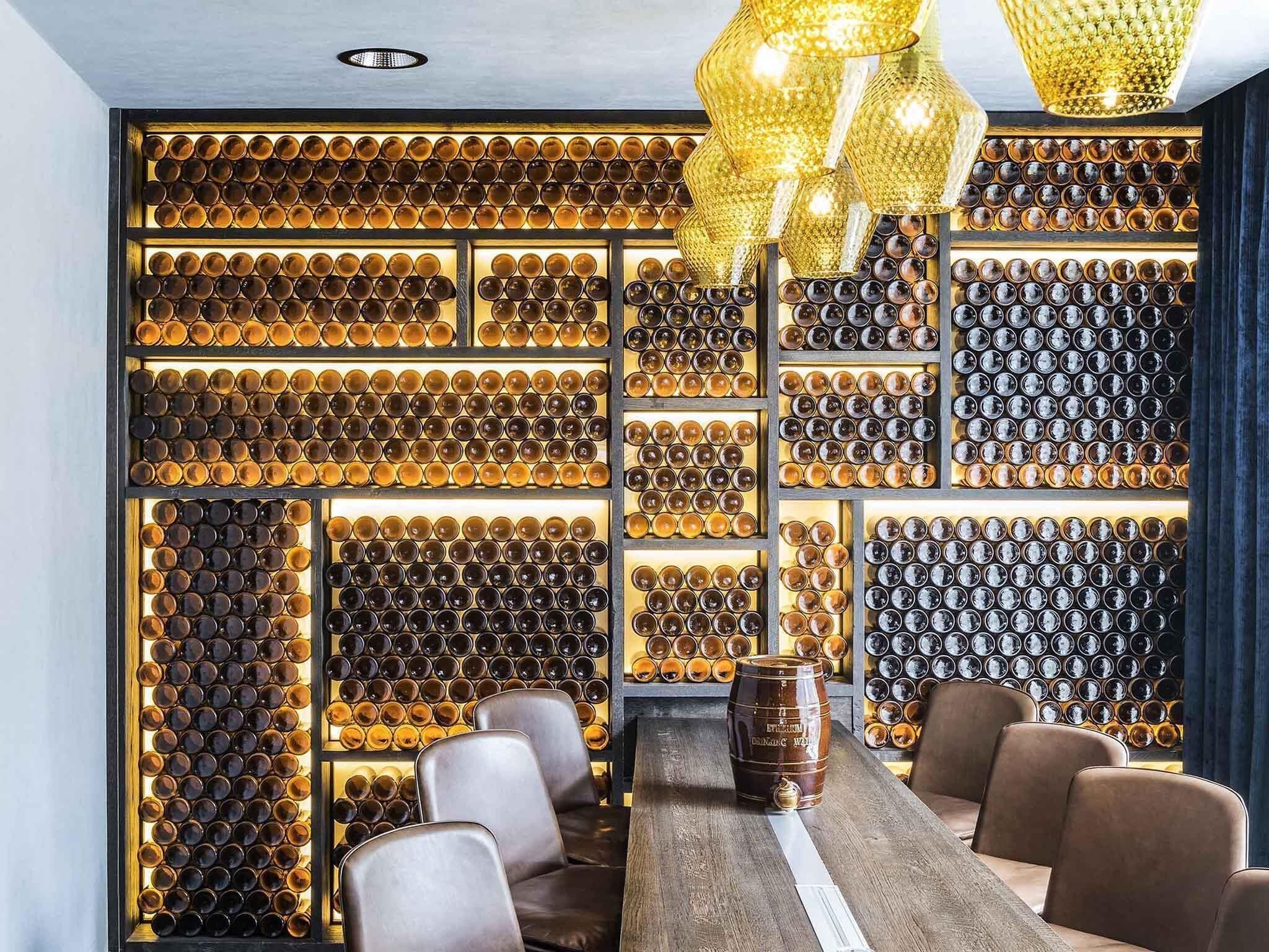 A bar area with a long wooden counter, multiple seating arrangements, and a wall of illuminated bottles.