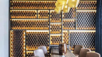 Un espace bar doté d’un long comptoir en bois, de plusieurs types de sièges et d’un mur décoré de bouteilles illuminées.