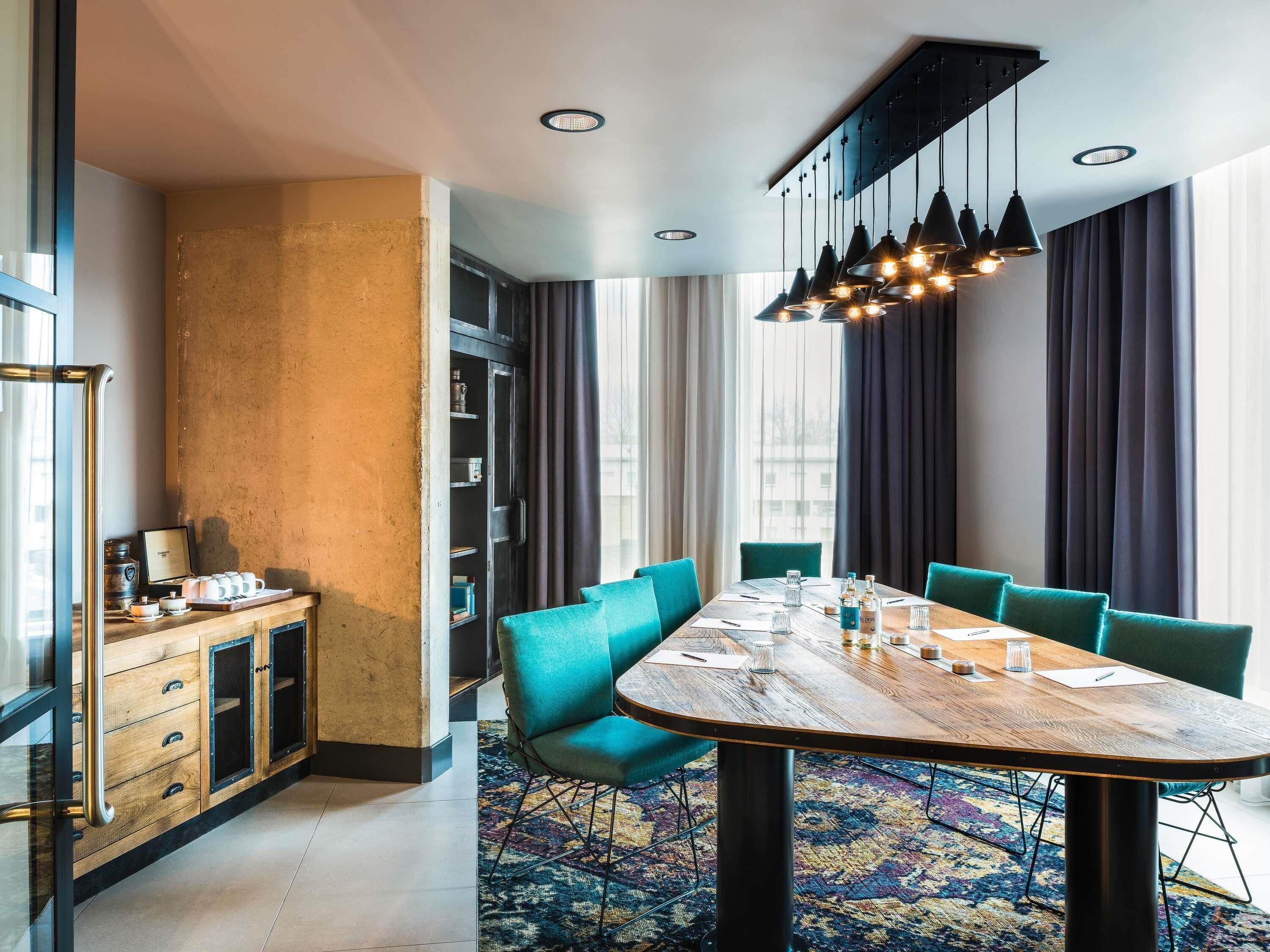 A modern dining area with a wooden table, teal chairs, and a patterned rug.