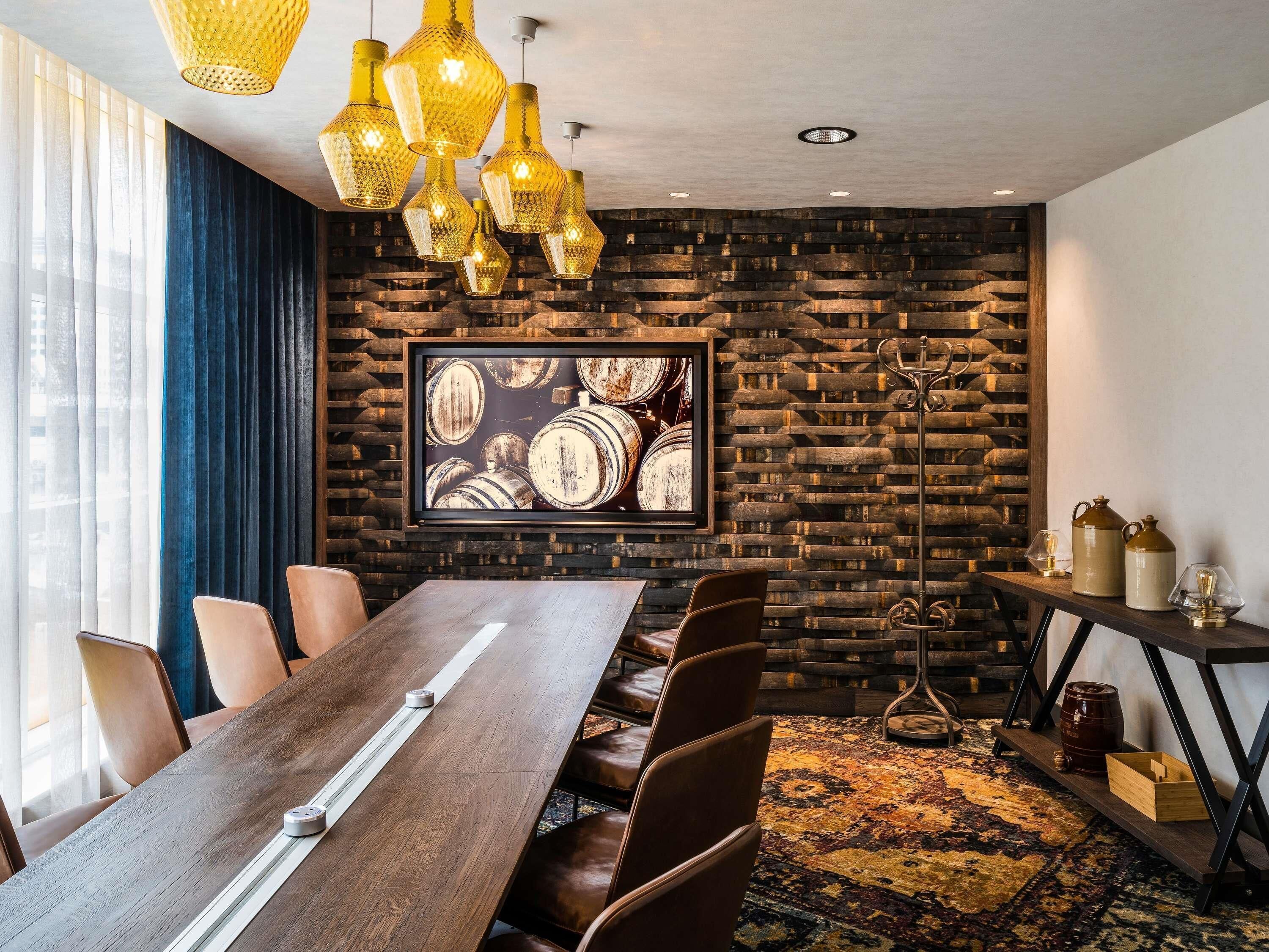 Una sala de conferencias con una larga mesa de madera, sillas de cuero, un tapete estampado y una obra de arte en la pared que representa barriles.