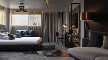 A modern hotel room with a large bed, a sofa, a desk, and a dining area.