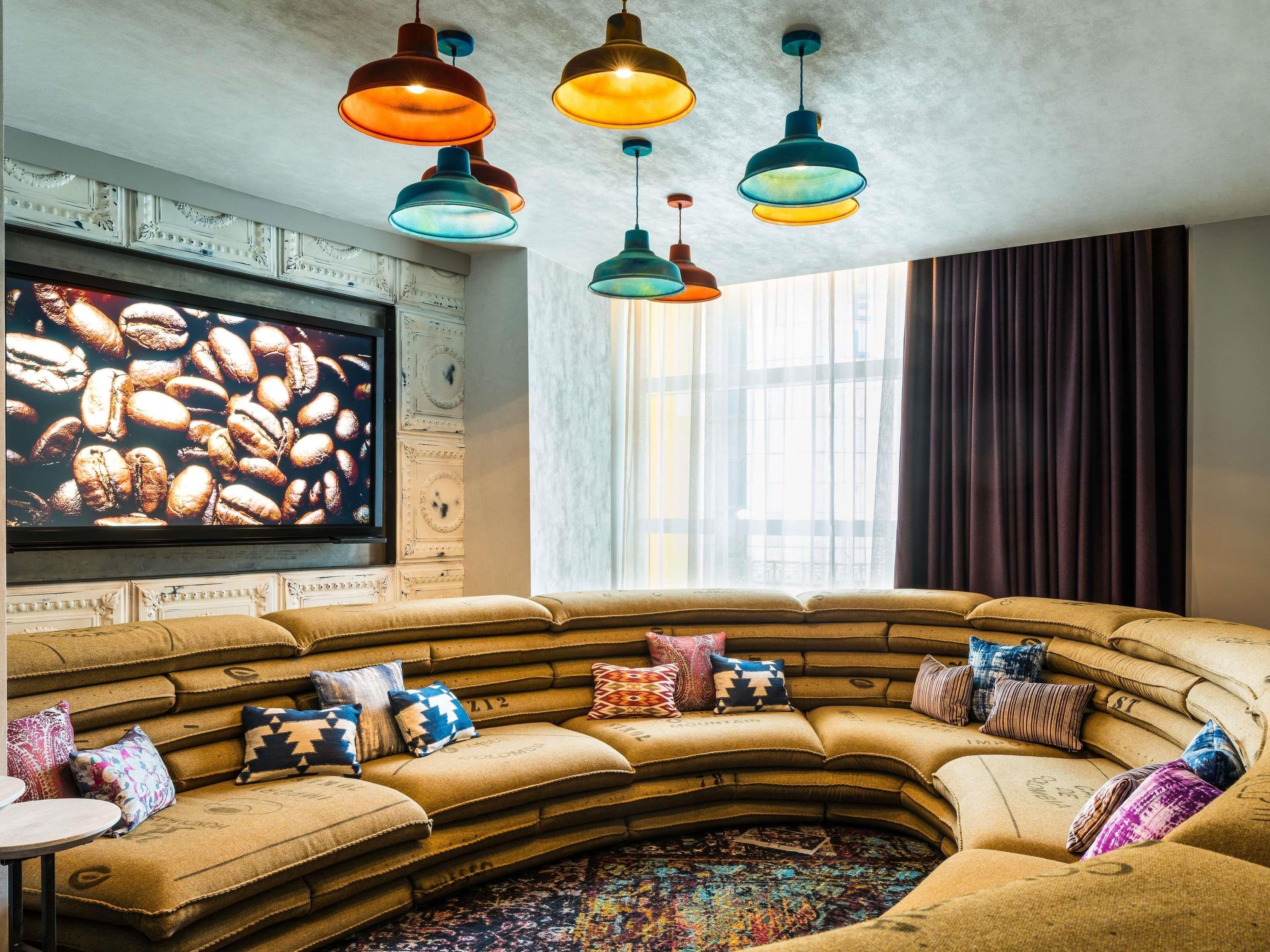 Ein gemütliches Wohnzimmer mit einem gebogenen Ecksofa, farbenfrohen Kissen und einer großen Wandkunst mit Kaffeebohnen-Motiv.
