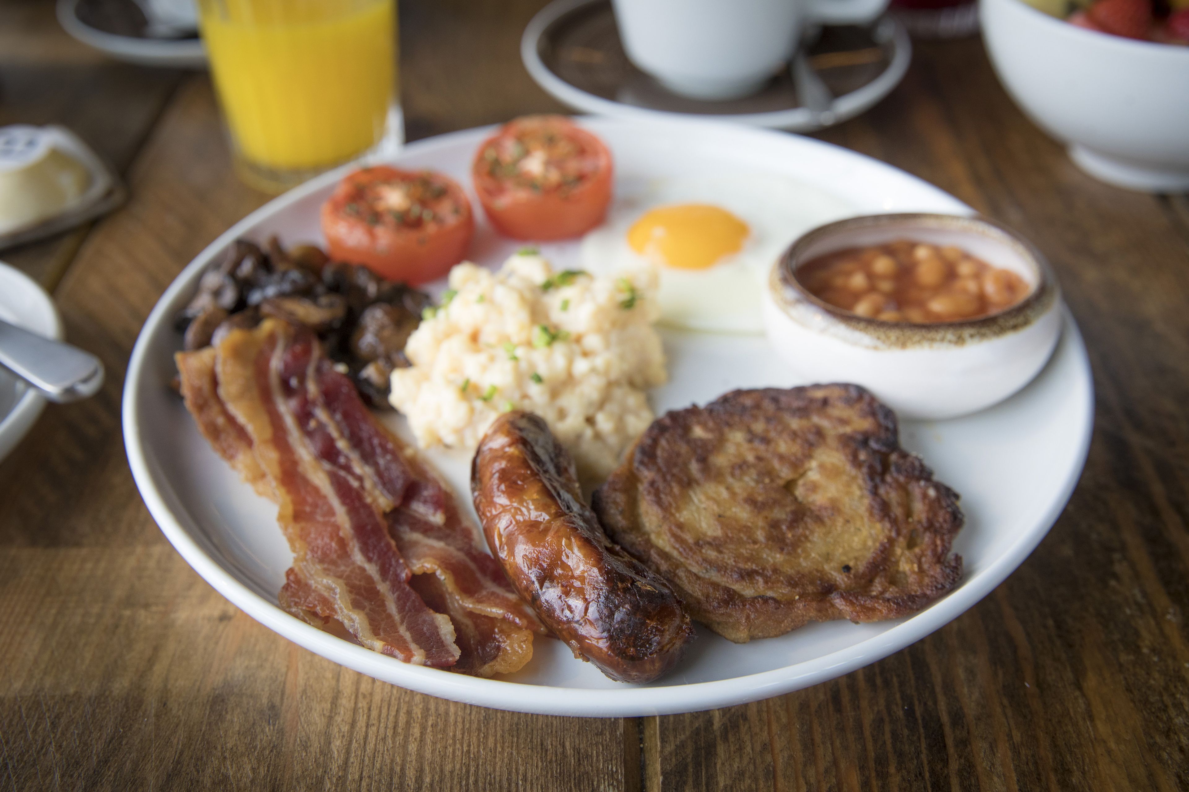 A plate of breakfast food including bacon, sausages, eggs, tomatoes, beans, and toast.
