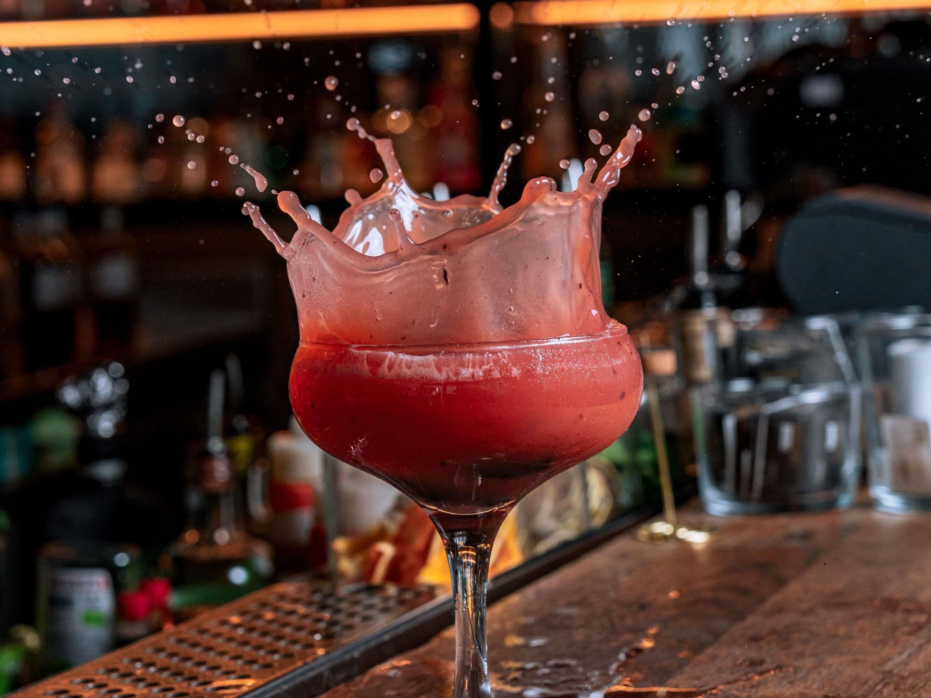 Un verre contenant un liquide rouge et quelques gouttes, posé sur le comptoir d’un bar.