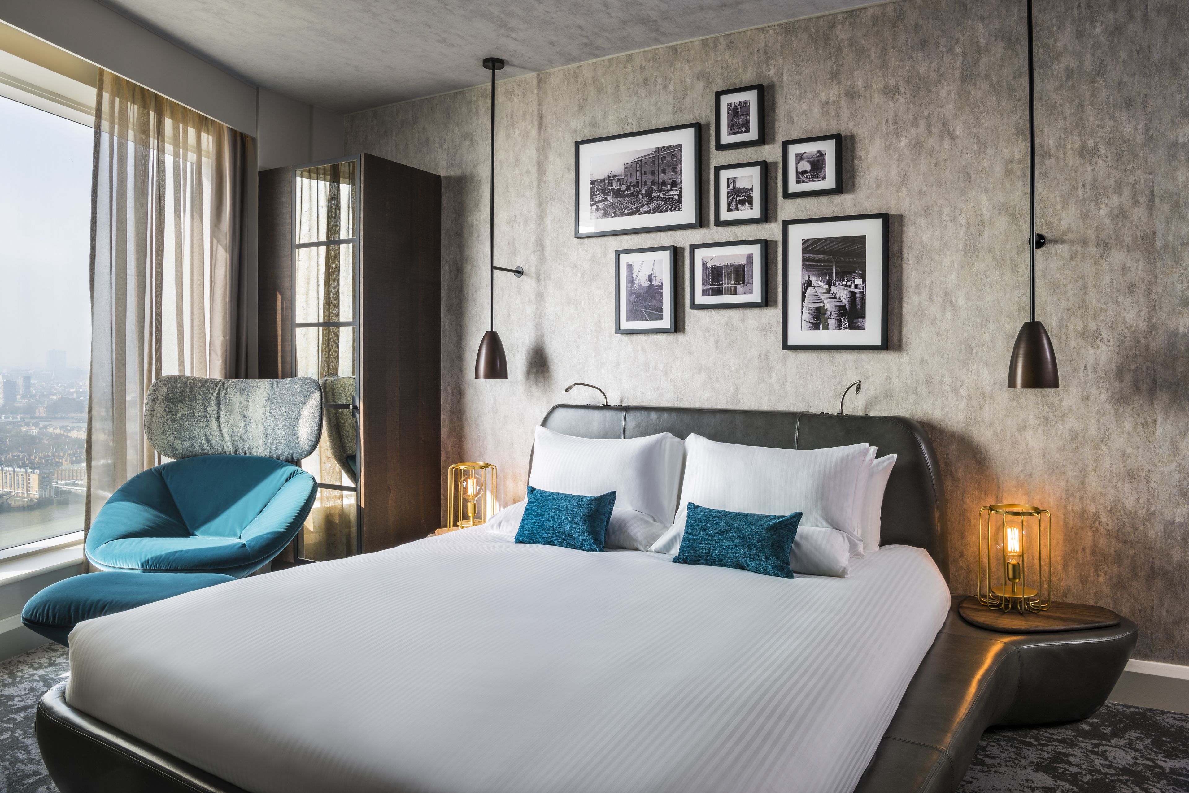 Habitación de hotel moderna con una cama grande, un sillón azul y vista a la ciudad.