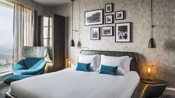 A modern hotel room with a large bed, a blue armchair, and a city view.