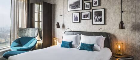 Habitación de hotel moderna con una cama grande, un sillón azul y vista a la ciudad.