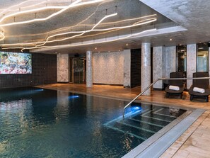 Ein moderner Poolbereich im Innenbereich mit klarem Wasser, einer Lounge mit Sesseln und einem großen, abstrakten Kunstwerk an der Wand.