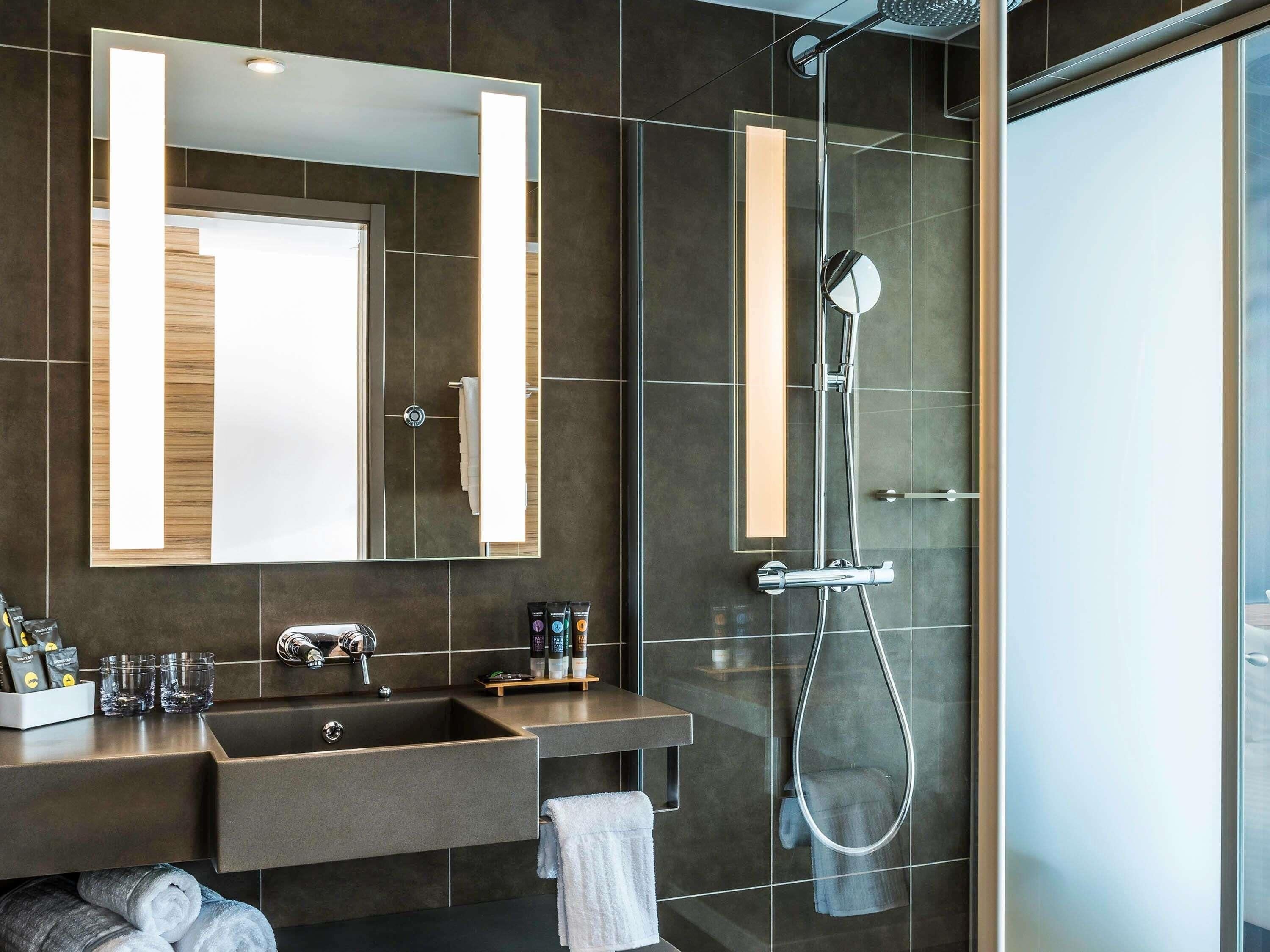 A modern bathroom with a large mirror, a shower, and a sink with toiletries.