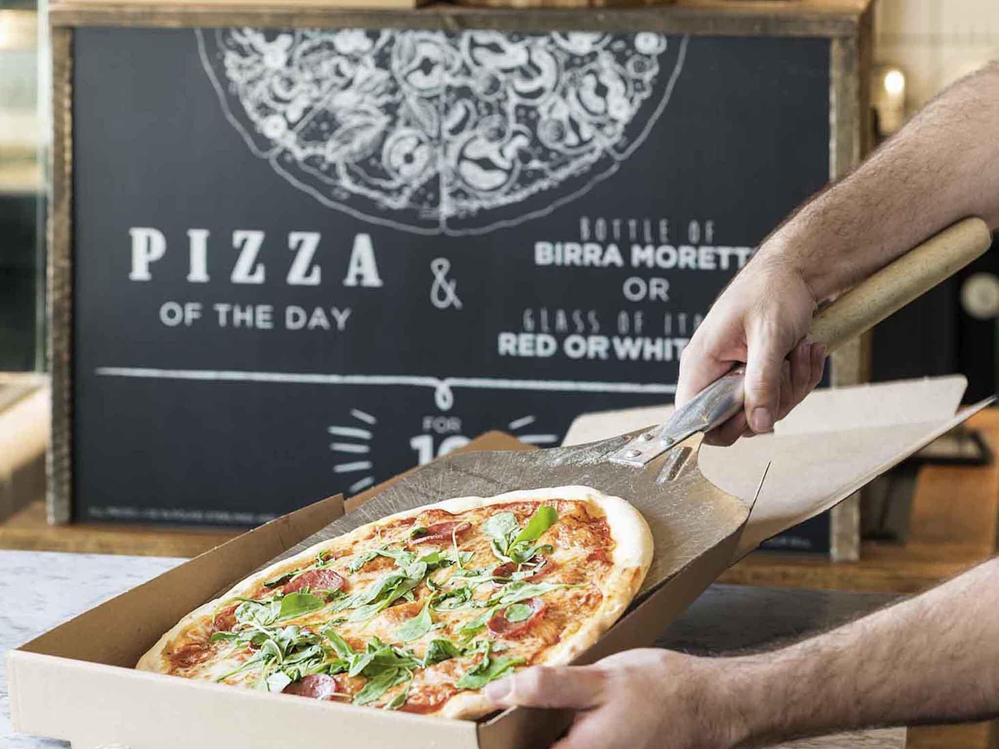 Pizza recién servida de una caja, con un cartel al fondo.