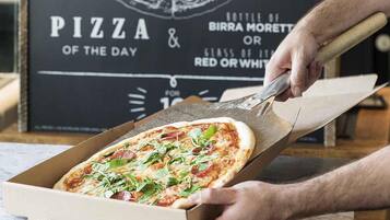 Pizza recién servida de una caja, con un cartel al fondo.